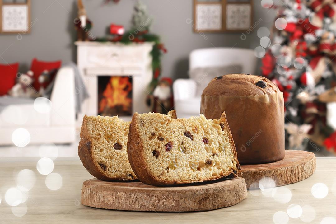 Fatia de panetone com frutas cristalizadas em casa com decoração de Natal ao fundo.