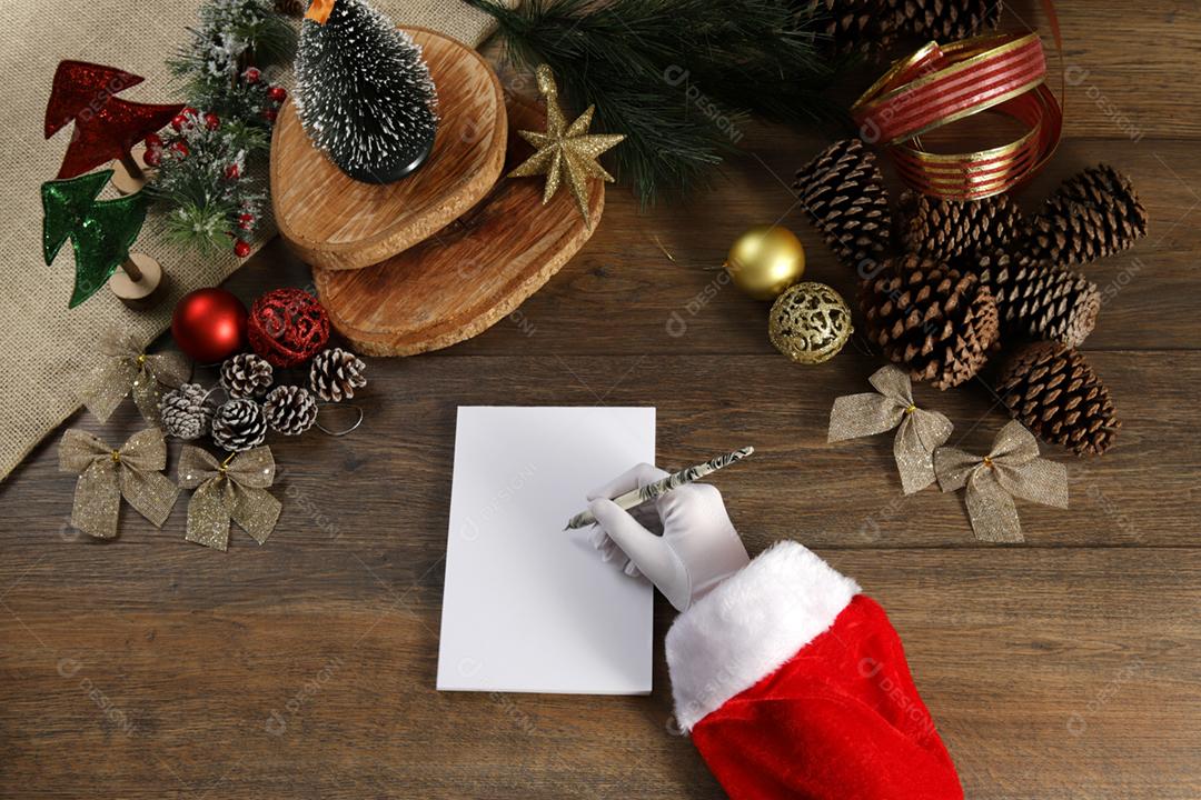 Vista superior da mão do papai noel escrevendo uma carta na mesa de madeira.