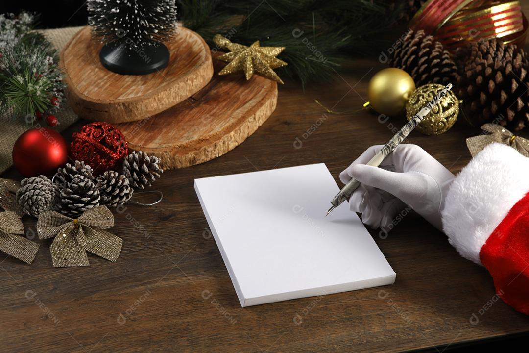 A mão do Papai Noel escrevendo uma carta na mesa de madeira.