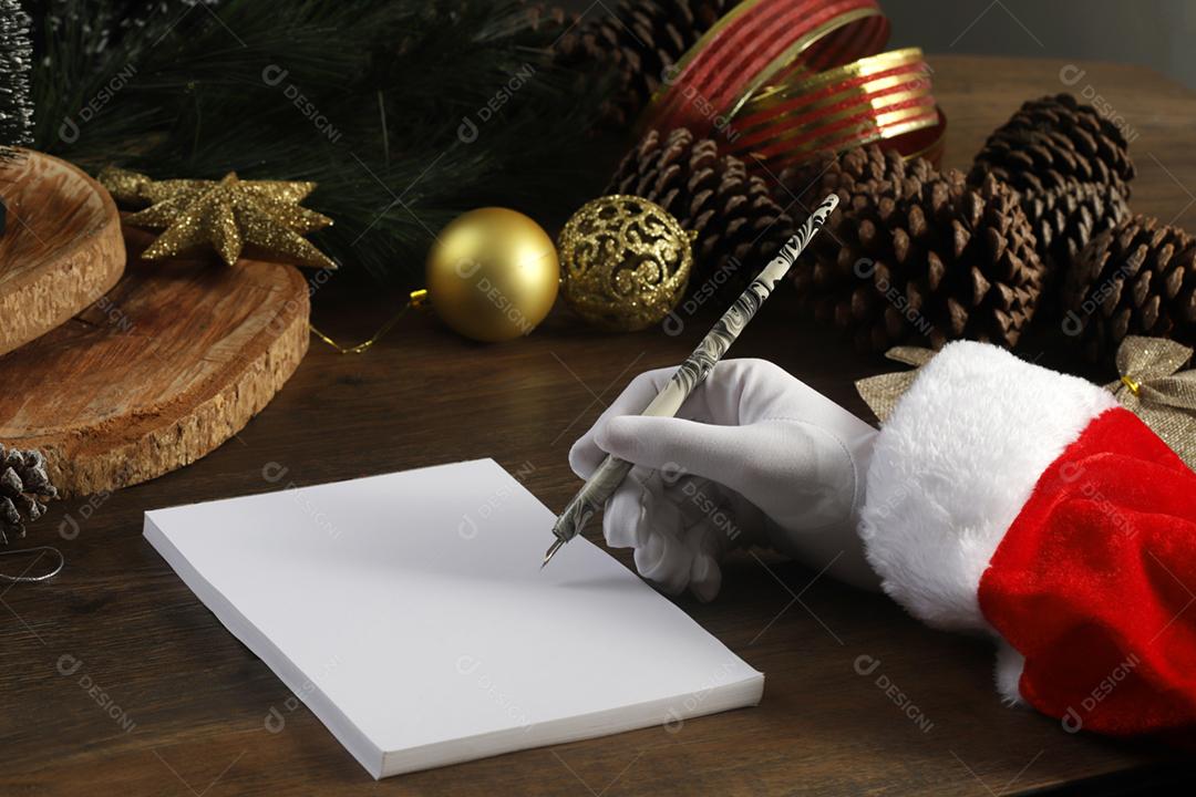 A mão do Papai Noel escrevendo uma carta na mesa de madeira.