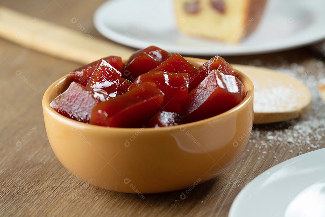 lata amarela com geléia de goiaba cortada em cubos com goiabas ao fundo na mesa de madeira.