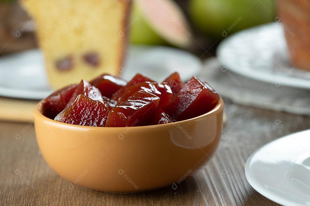 lata amarela com geléia de goiaba cortada em cubos com goiabas ao fundo na mesa de madeira.