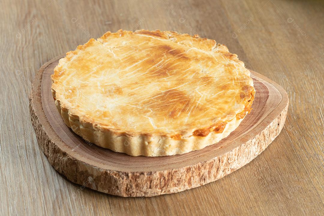 Feche o pedaço de torta de frango com requeijão, tomate, cebola e azeitonas na mesa de madeira e chapa branca.