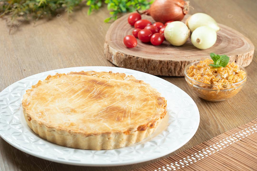 Feche o pedaço de torta de frango com requeijão, tomate, cebola e azeitonas na mesa de madeira e chapa branca.