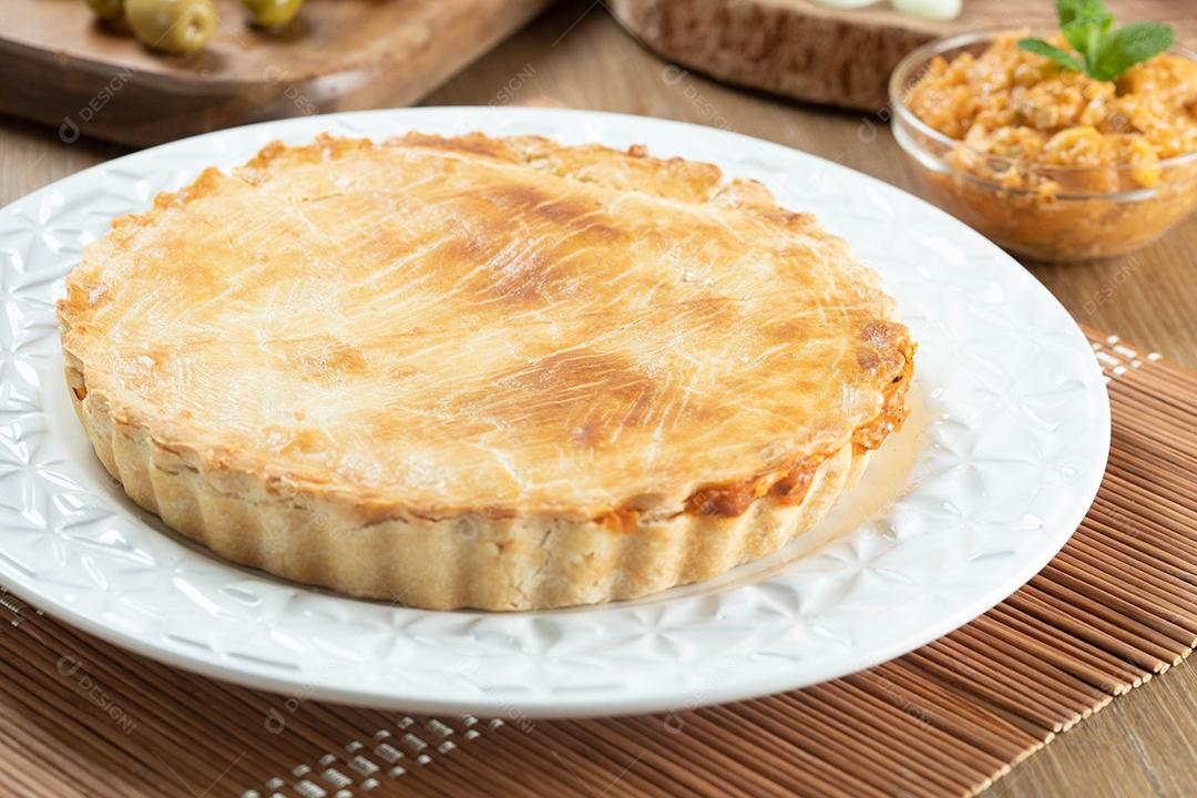 Feche o pedaço de torta de frango com requeijão, tomate, cebola e azeitonas na mesa de madeira e chapa branca.