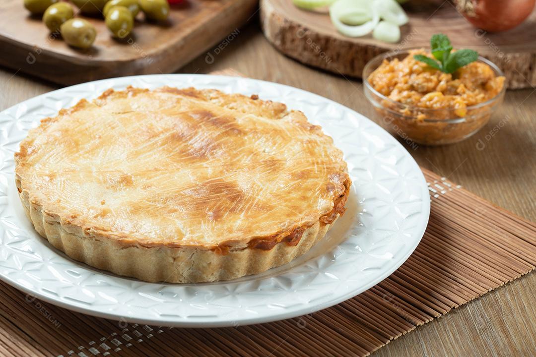 Feche o pedaço de torta de frango com requeijão, tomate, cebola e azeitonas na mesa de madeira e chapa branca.