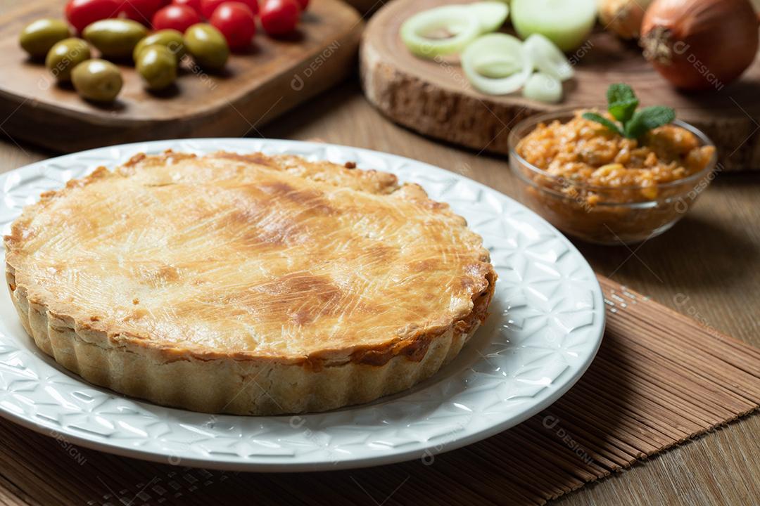 Feche o pedaço de torta de frango com requeijão, tomate, cebola e azeitonas na mesa de madeira e chapa branca.