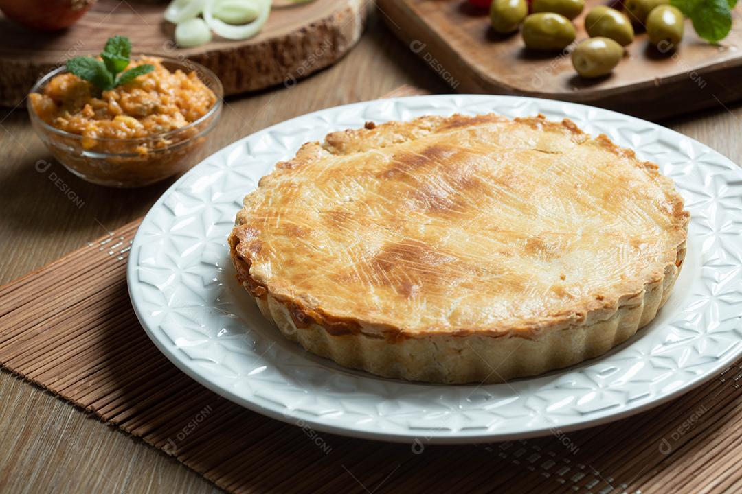 Feche o pedaço de torta de frango com requeijão, tomate, cebola e azeitonas na mesa de madeira e chapa branca.