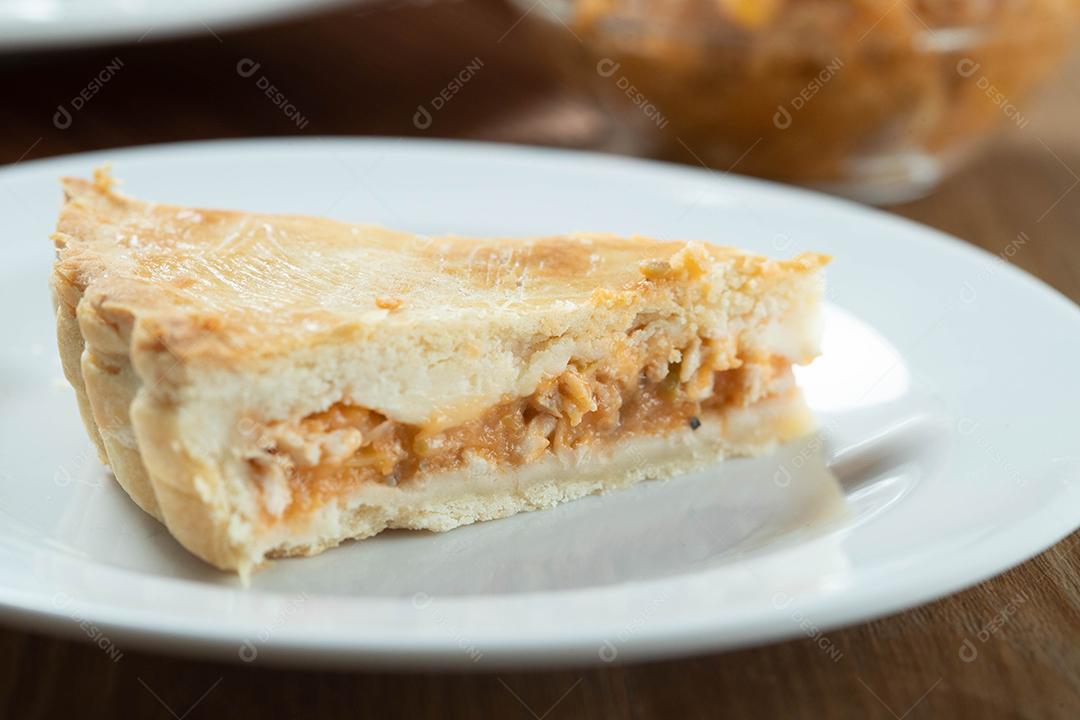 Feche o pedaço de torta de frango com requeijão, tomate, cebola e azeitonas na mesa de madeira e chapa branca.