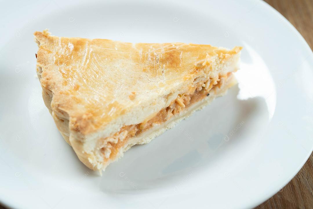 Feche o pedaço de torta de frango com requeijão, tomate, cebola e azeitonas na mesa de madeira e chapa branca.