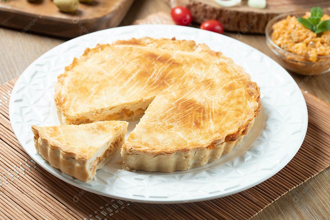 Feche o pedaço de torta de frango com requeijão, tomate, cebola e azeitonas na mesa de madeira e chapa branca.