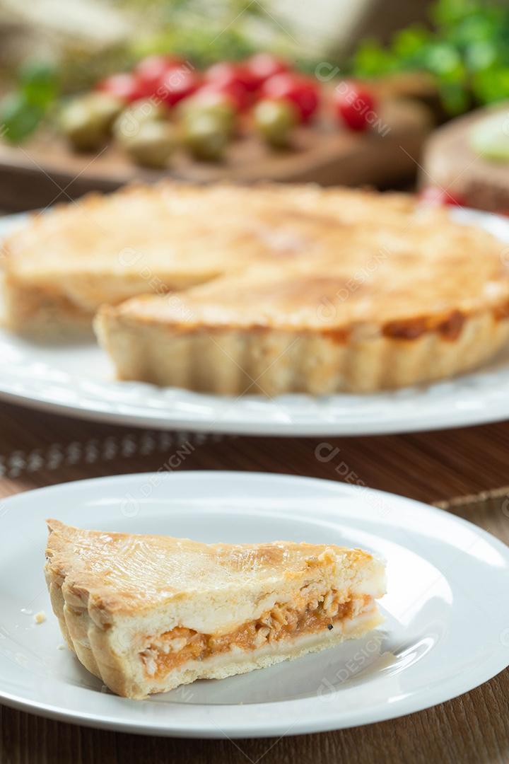 Feche o pedaço de torta de frango com requeijão, tomate, cebola e azeitonas na mesa de madeira e chapa branca.