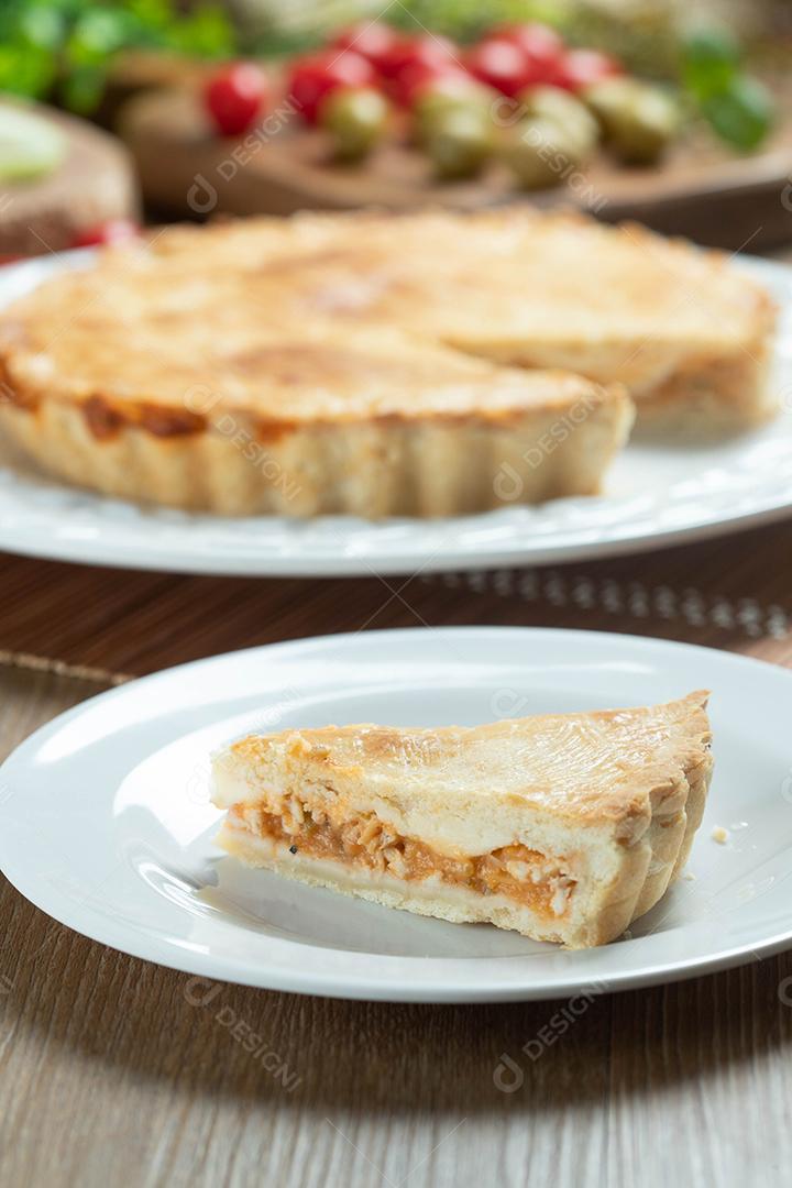 Feche o pedaço de torta de frango com requeijão, tomate, cebola e azeitonas na mesa de madeira e chapa branca.