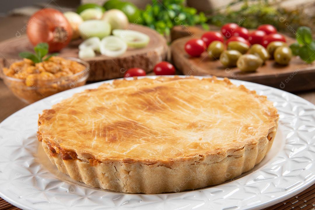 Torta de frango com requeijão, tomate, cebola e azeitonas na mesa de madeira e chapa branca. Vista do topo.