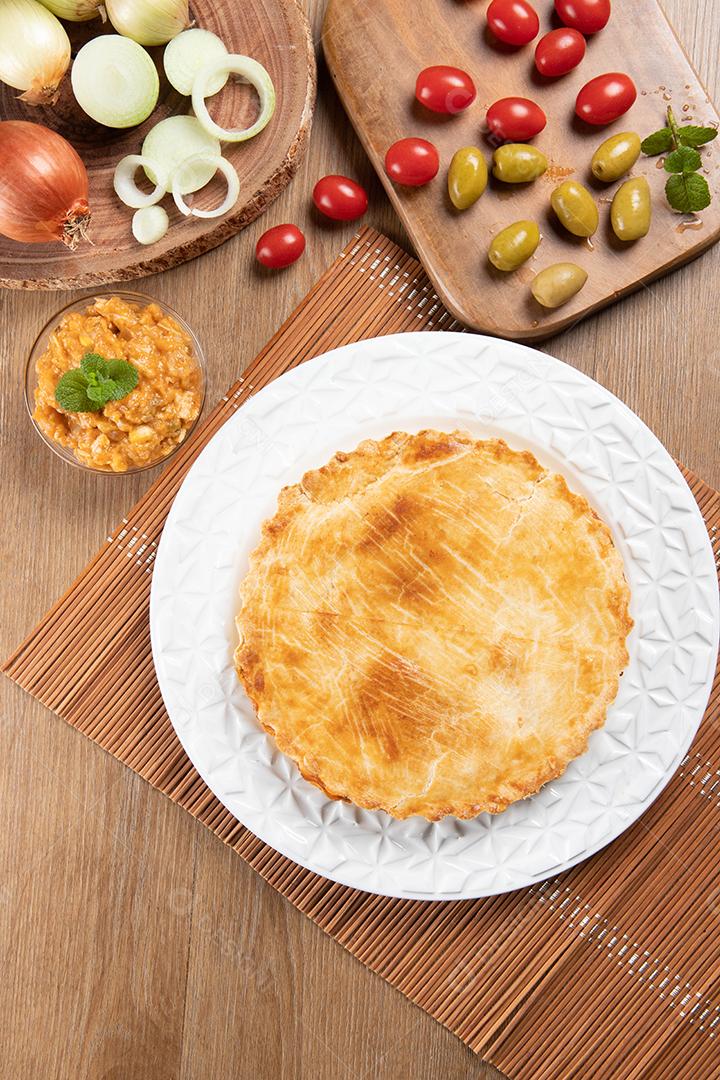 Torta de frango com requeijão, tomate, cebola e azeitonas na mesa de madeira e chapa branca. Vista do topo.