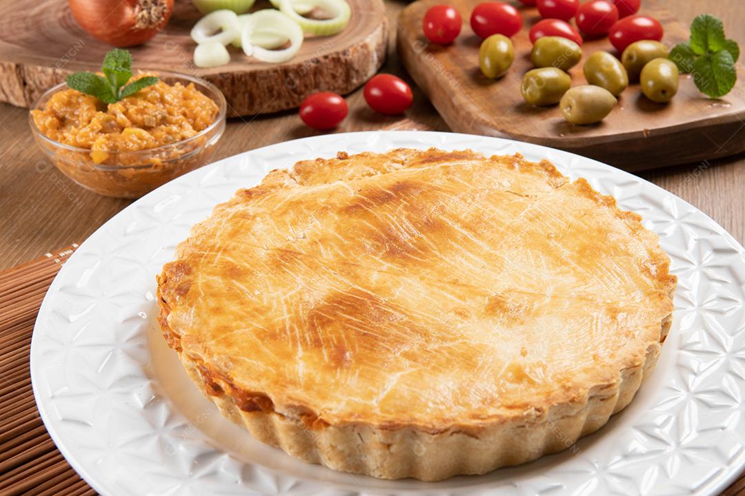 Torta de frango com requeijão, tomate, cebola e azeitonas na mesa de madeira e chapa branca. Vista do topo.