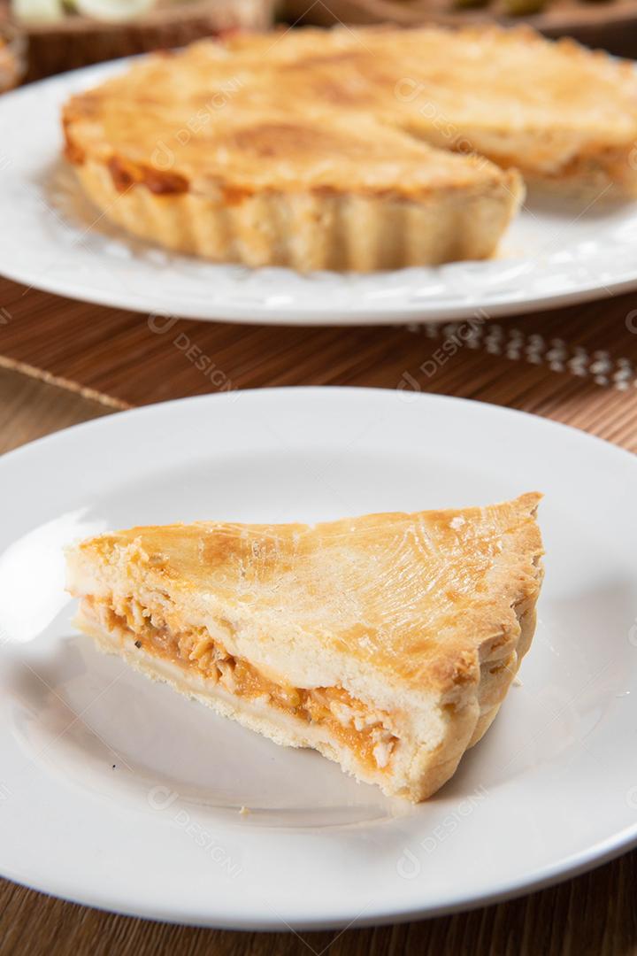 Feche o pedaço de torta de frango com requeijão, tomate, cebola e azeitonas na mesa de madeira e chapa branca.