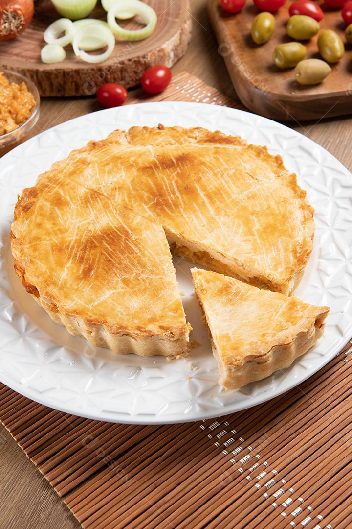 Torta de frango com requeijão, tomate, cebola e azeitonas na mesa de madeira e chapa branca.