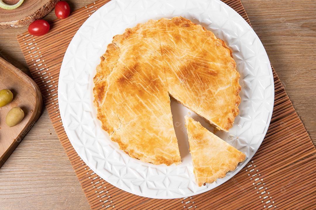 Torta de frango com requeijão, tomate, cebola e azeitonas na mesa de madeira e chapa branca. Vista do topo.