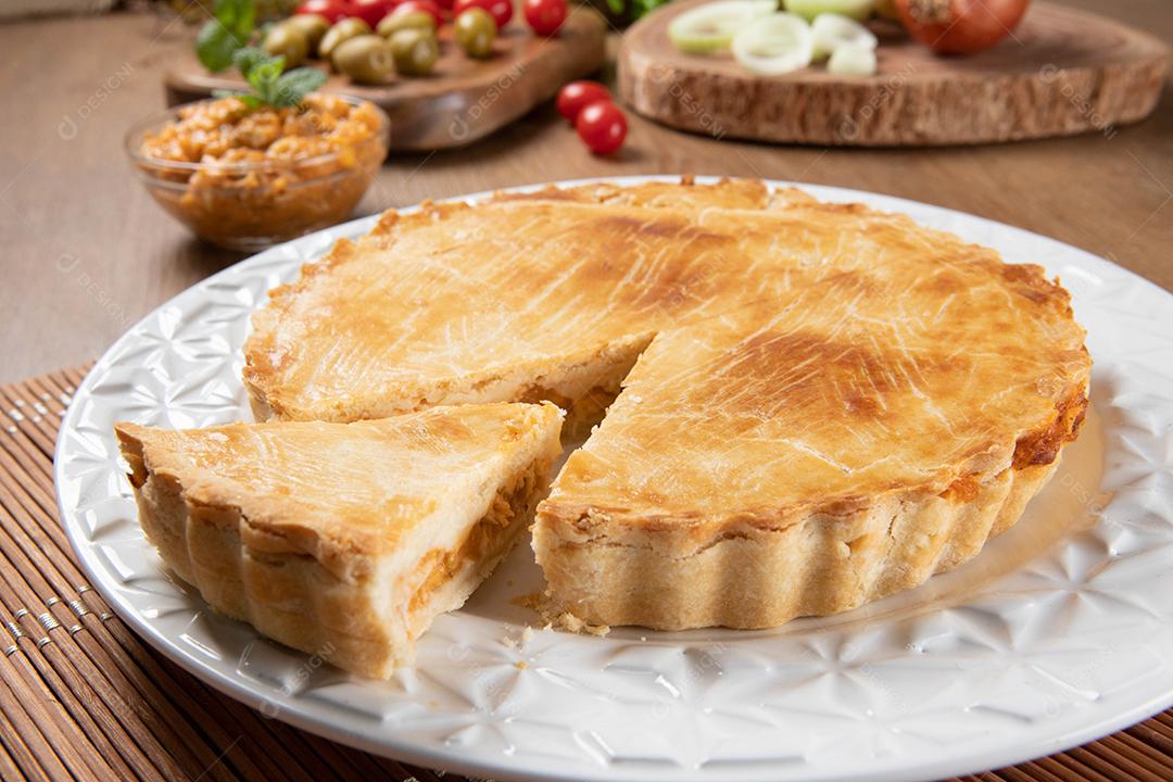 Feche o pedaço de torta de frango com requeijão, tomate, cebola e azeitonas na mesa de madeira e chapa branca.