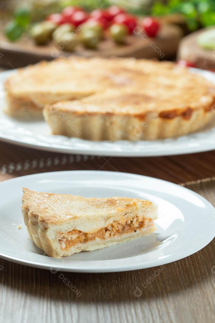 Feche o pedaço de torta de frango com requeijão, tomate, cebola e azeitonas na mesa de madeira e chapa branca.