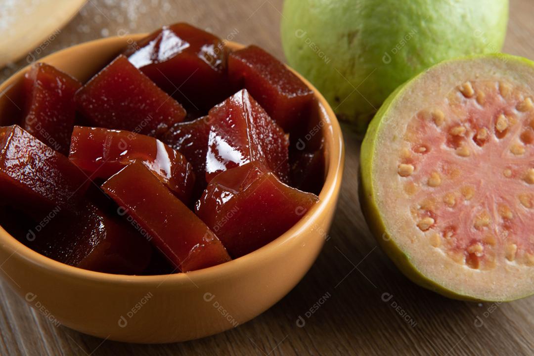 lata amarela com doce de goiaba cortada em cubos com goiabas atrás