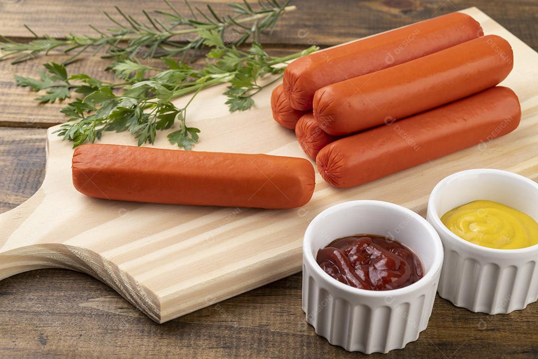 Salsichas sobre uma tábua de madeira com ketchup e mostarda.