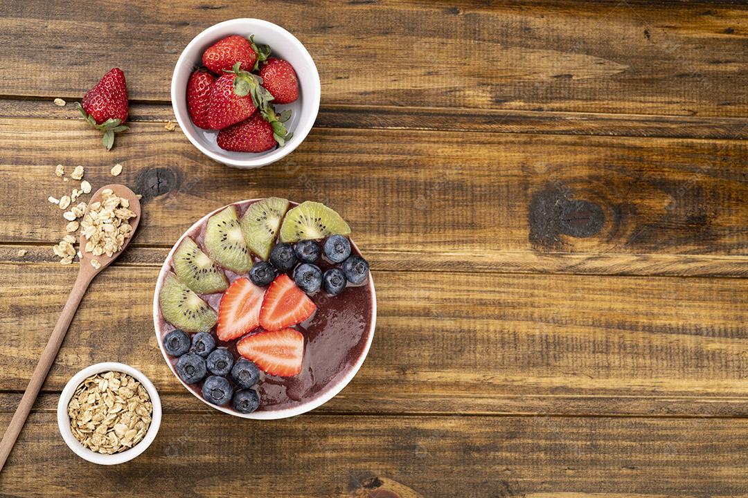 Tigela de açaí típica brasileira com frutas e muesli sobre fundo de madeira