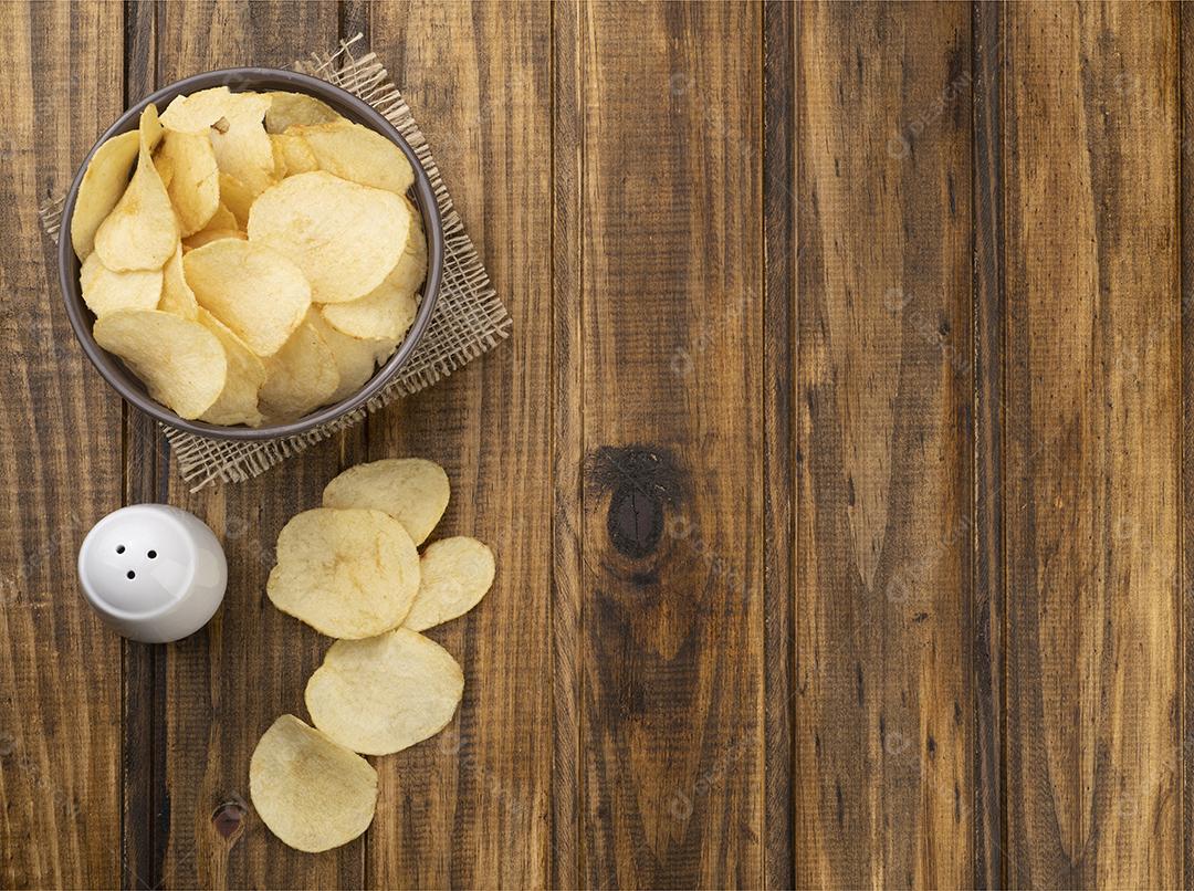 Batatas fritas em uma tigela e sal sobre a mesa de madeira