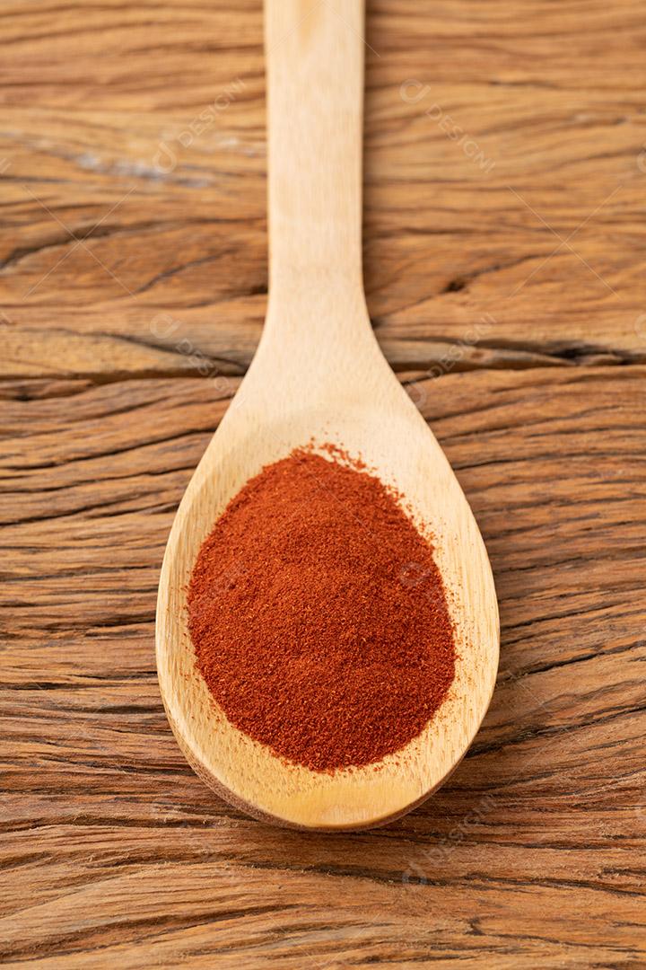 pimenta páprica vermelha em uma colher sobre a mesa de madeira.