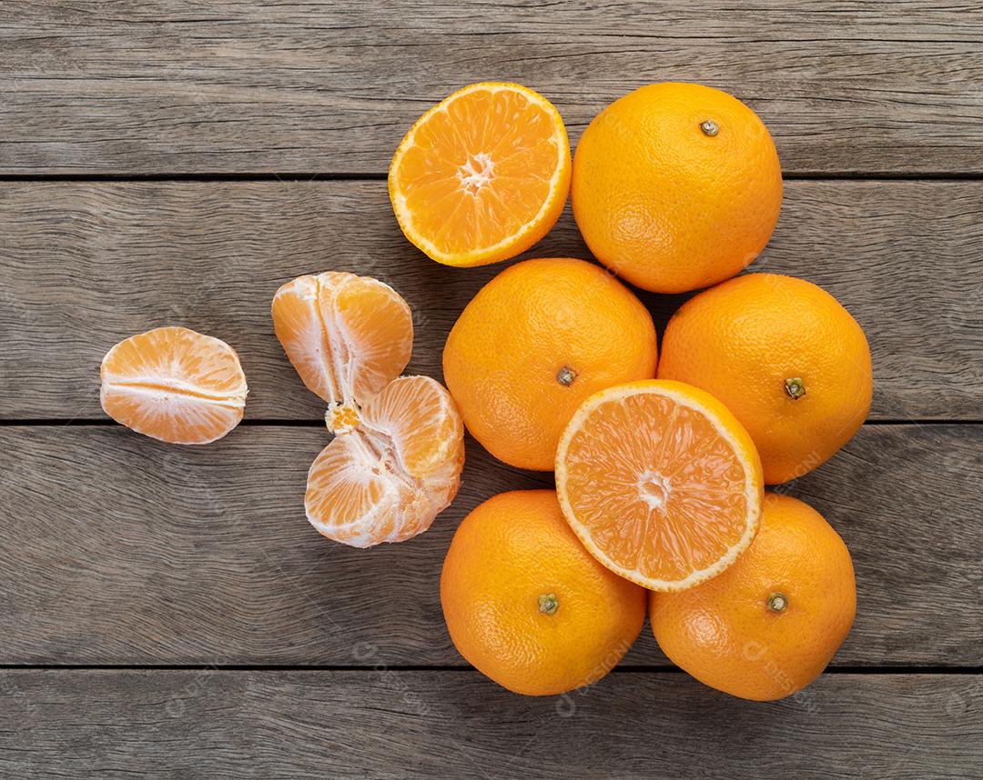 Tangerinas com frutas cortadas sobre a mesa de madeira.