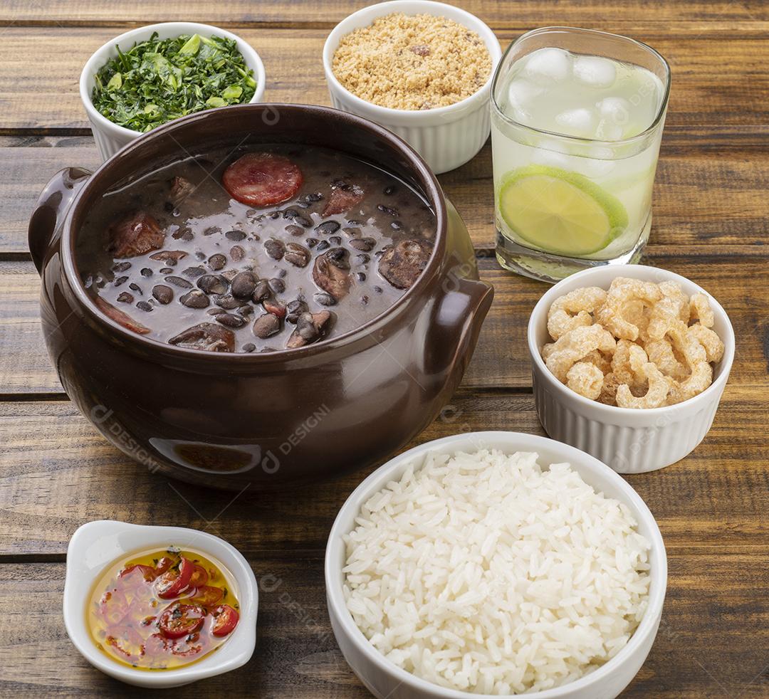 Feijoada tradicional brasileira com couve, arroz, torresmo, farinha de mandioca e caipirinha.