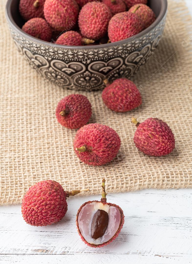 Lichias em uma tigela com frutas cortadas sobre a mesa de madeira.