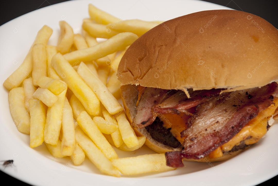 Hambúrguer com queijo derretido, maionese, alface batata frita prato branco