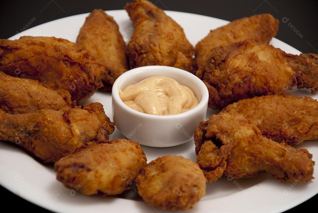 Coxas de frango empanadas e fritas sobre prato branco molho