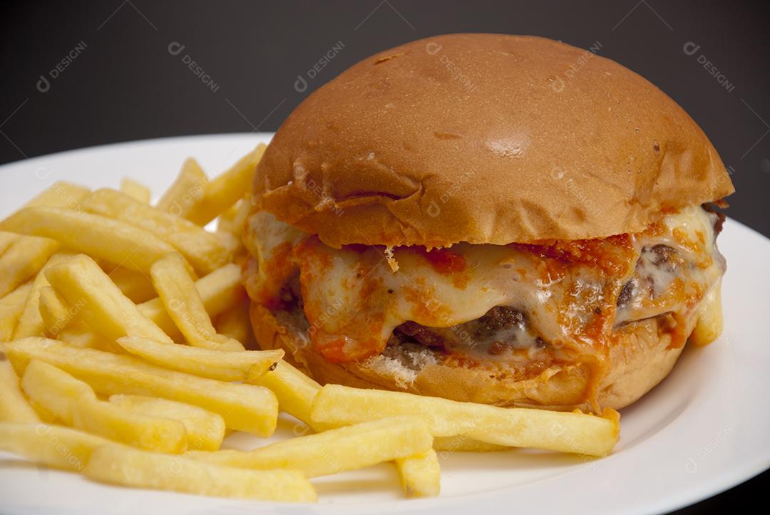 Hambúrguer com queijo derretido, maionese, alface batata frita prato branco