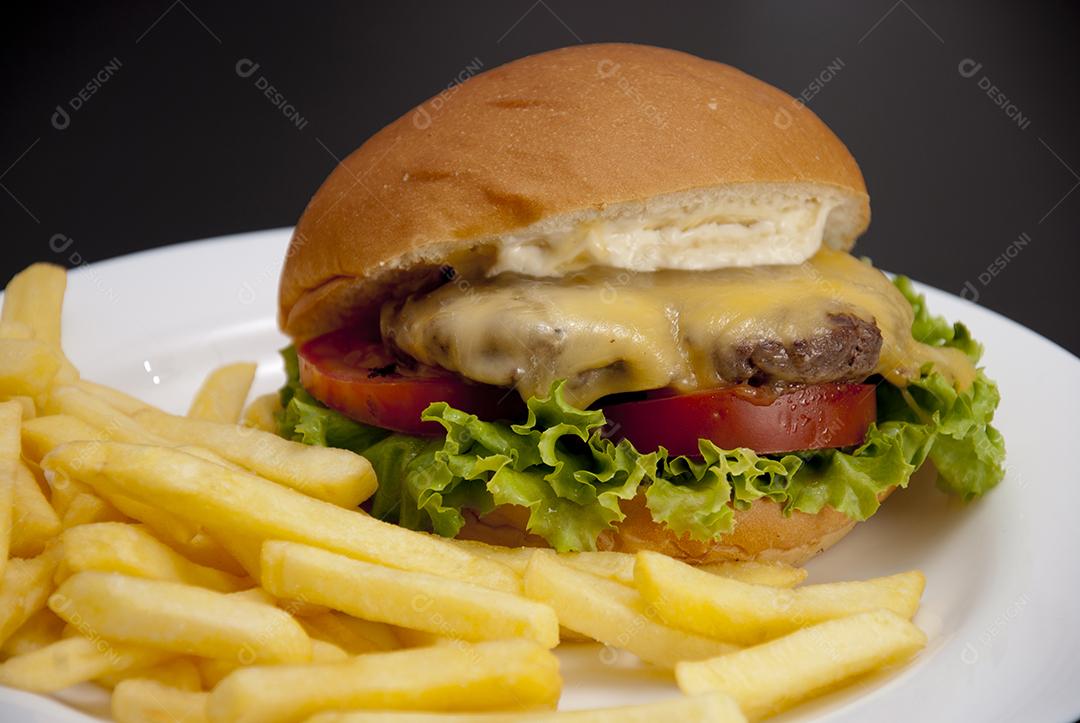 Hambúrguer com queijo derretido, maionese, alface batata frita prato branco