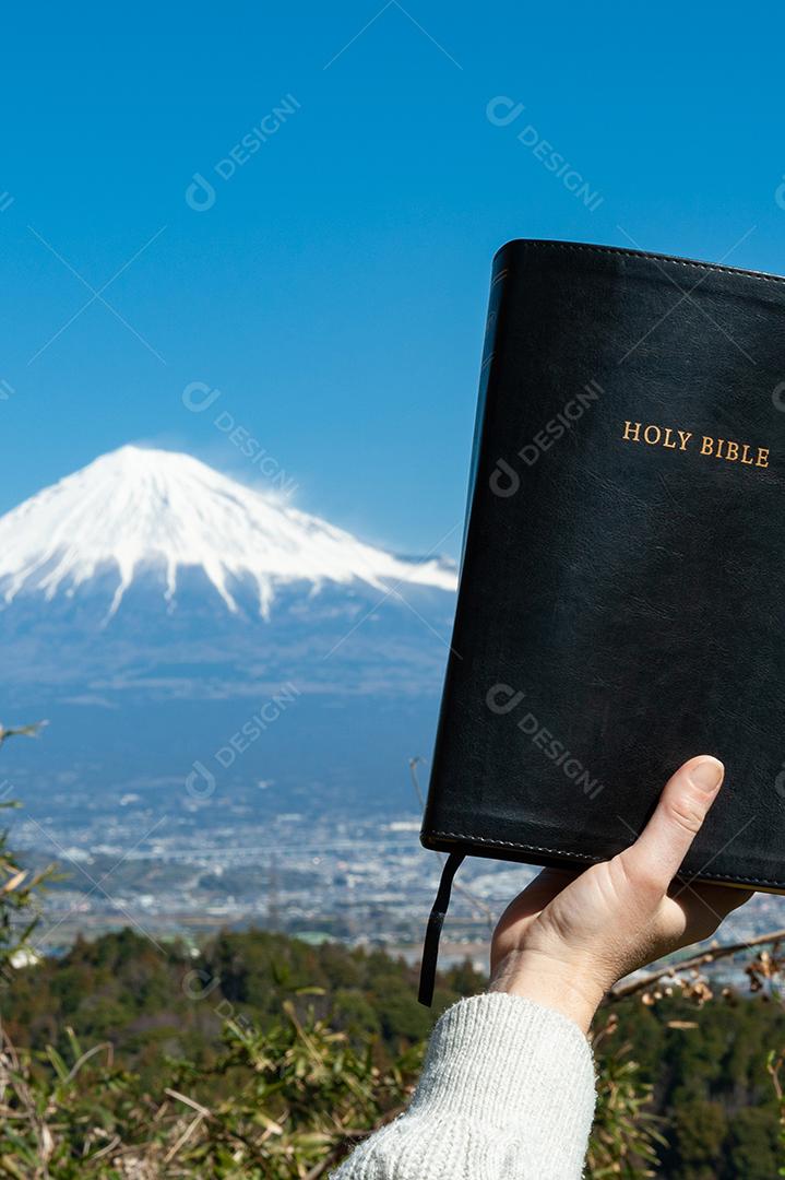 Mão levantada segurando a Bíblia Sagrada em frente ao Monte Fuji no Japão.