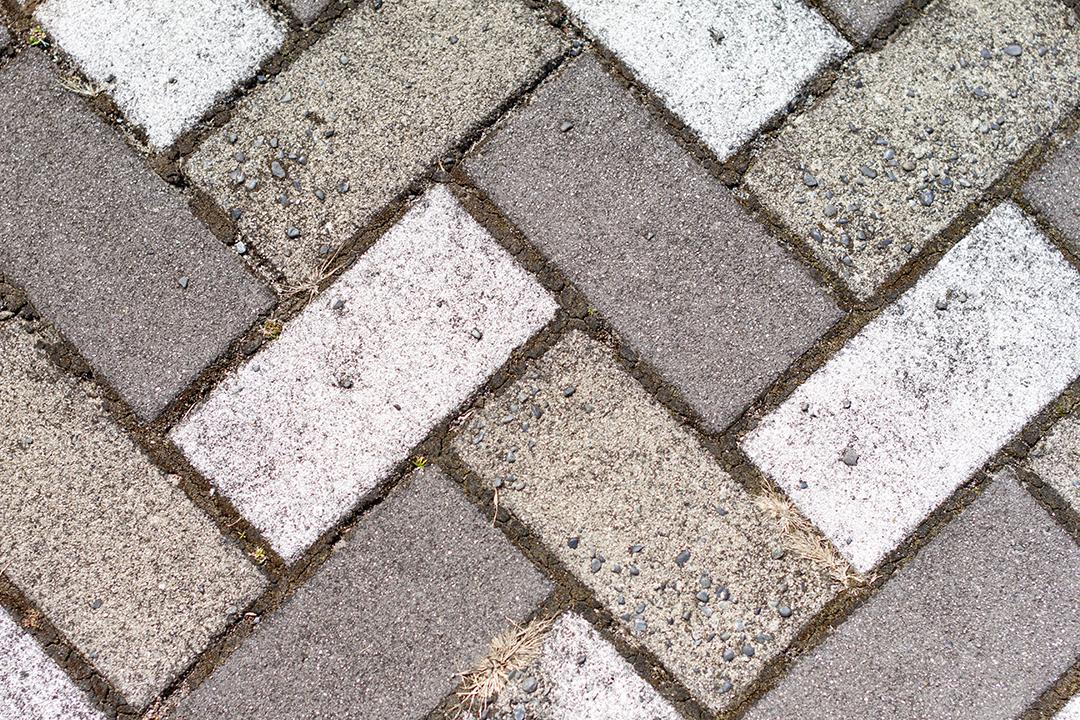 Calçada pavimentada com azulejos retangulares brancos e cinza em vista superior.