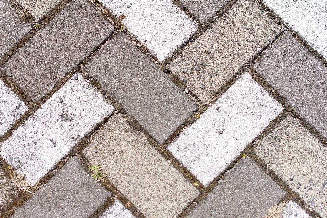 Calçada pavimentada com azulejos retangulares brancos e cinza em vista superior.