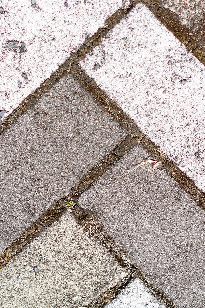 Calçada pavimentada com azulejos retangulares brancos e cinza em vista superior.