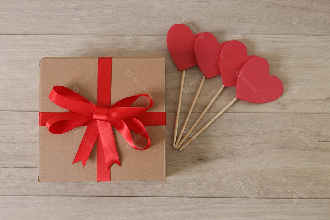 Caixa de presente marrom com fita vermelha e corações.