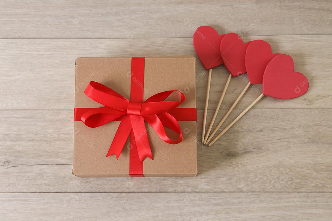 Caixa de presente marrom com fita vermelha e corações.