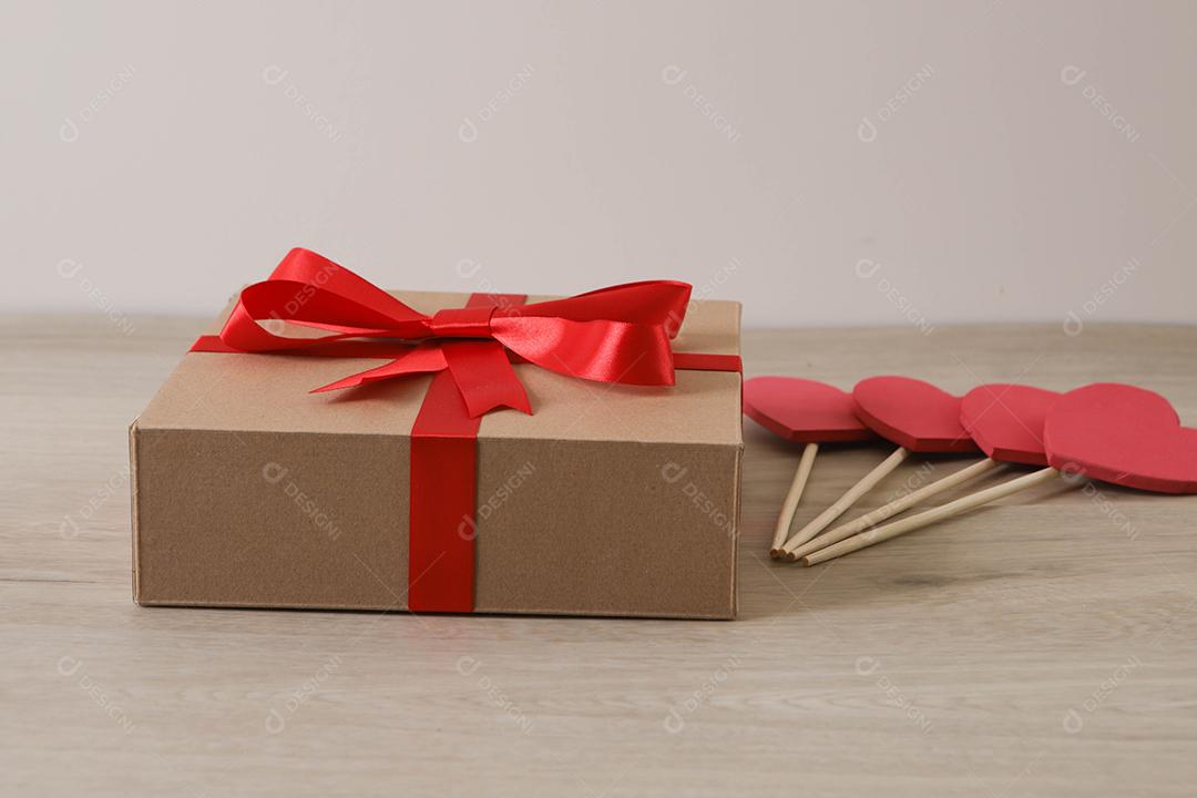 Caixa de presente marrom com fita vermelha e corações.