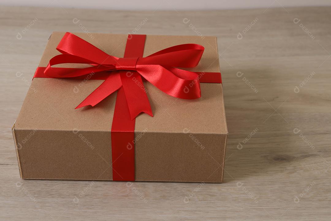 Caixa de presente marrom com fita vermelha em fundo de madeira