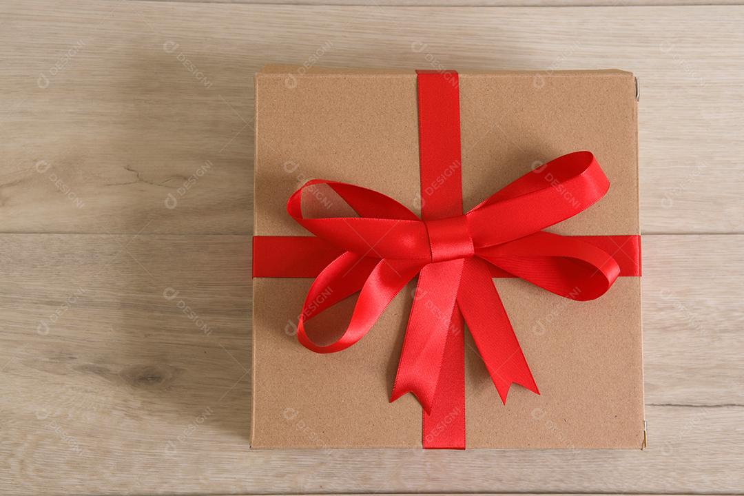 Caixa de presente marrom com fita vermelha em fundo de madeira
