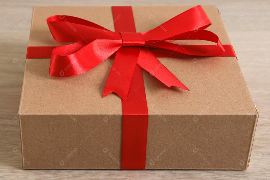 Caixa de presente marrom com fita vermelha em fundo de madeira