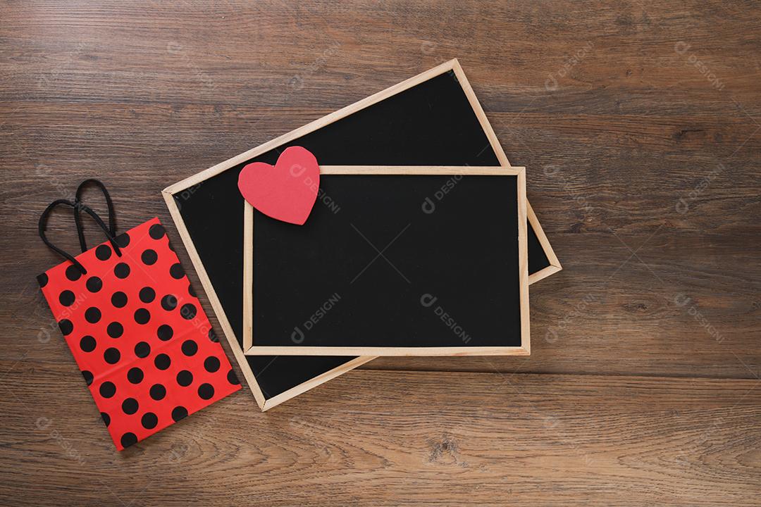 quadro-negro com sacola de compras, presente e corações em fundo de madeira