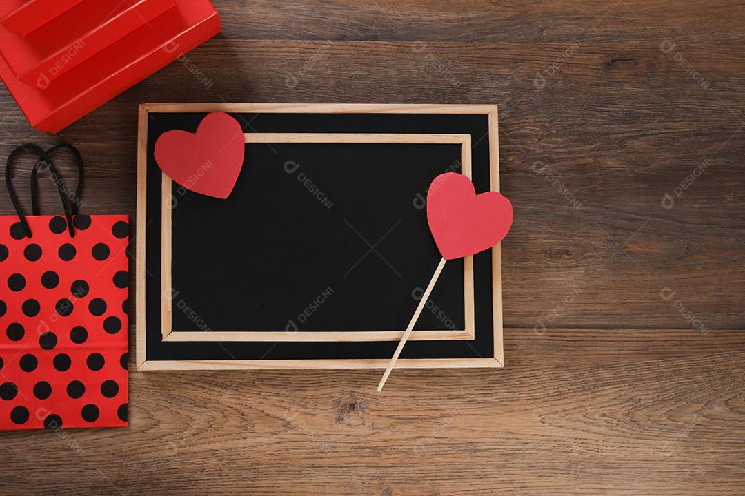 quadro-negro com sacola de compras, presente e corações em fundo de madeira