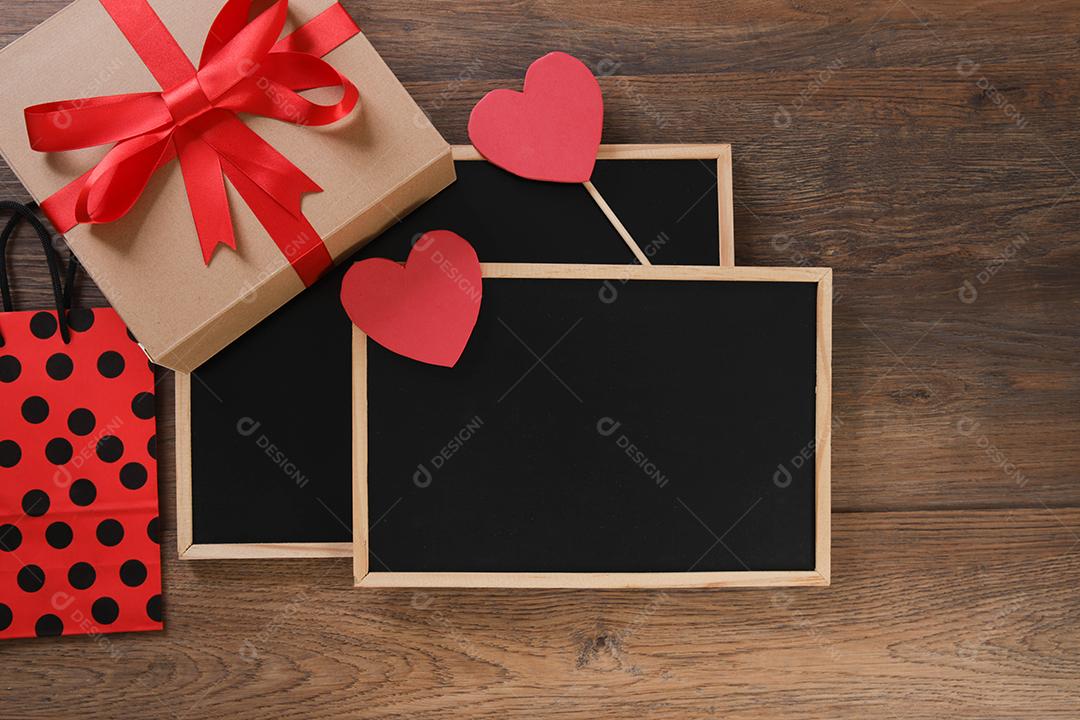 quadro-negro com sacola de compras, presente e corações em fundo de madeira